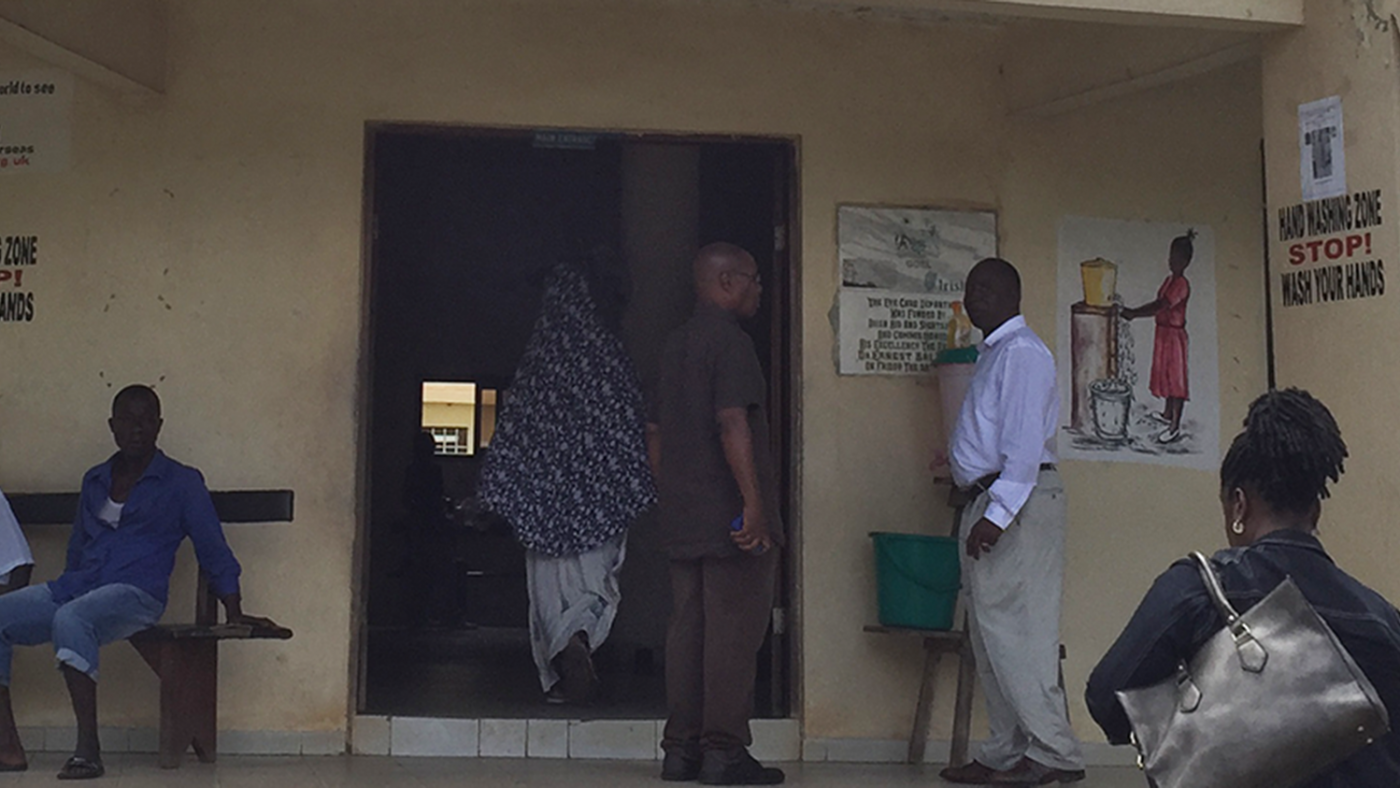 A women is walking up to the entrance of a building. Men stand around outside.