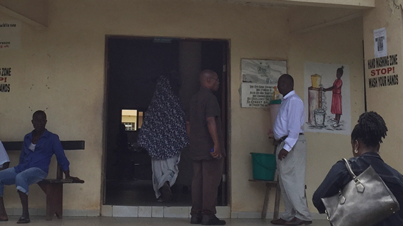 A women is walking up to the entrance of a building. Men stand around outside.