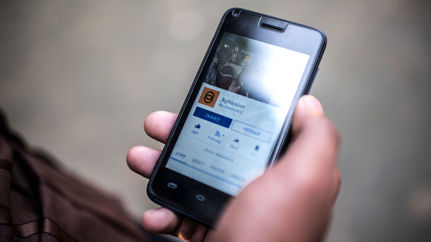 A photo of a phone in Sisan's hand. On the screen is Sightsavers' Facebook page.