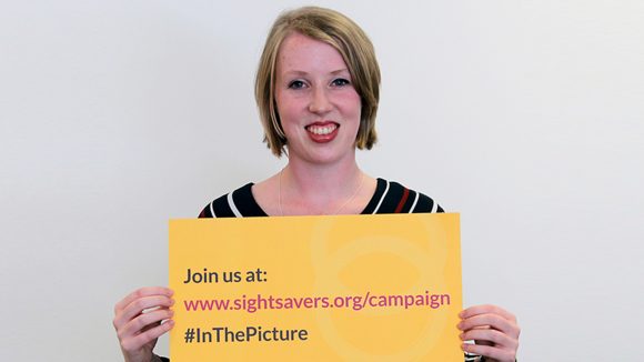 Paralympian Georgie Bullen holds a yellow sign containing the words: 'Join us at en.sightsavers.co/campaign, #inthepicture'.