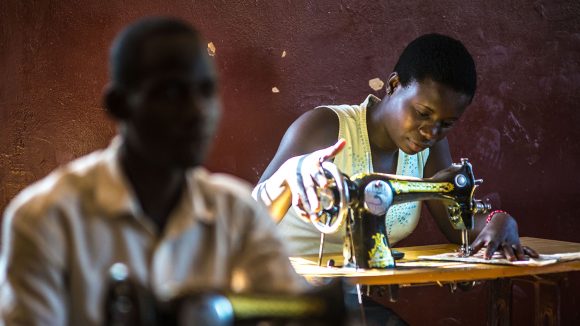 A lady is sitting using a sewing machine in a dark room.