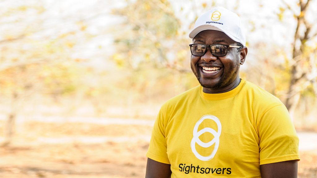 A man smiles, wearing a yellow Sightsavers tshirt.
