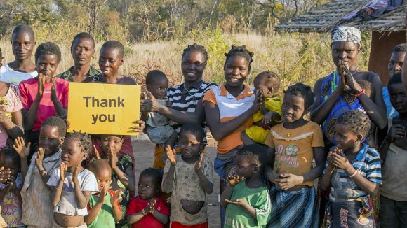 In Mozambique, a group of villagers smile and hold up a yellow sign saying 'thank you'.