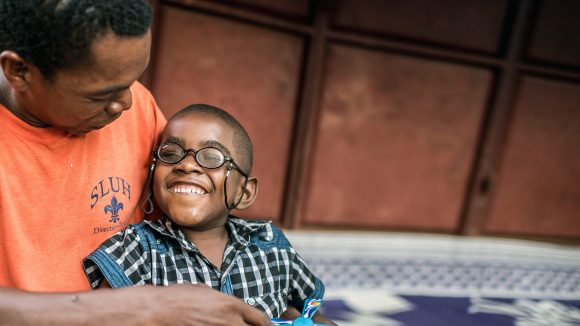 Five-year-old Saidi smiles while sitting on his father's lap following cataract surgery.
