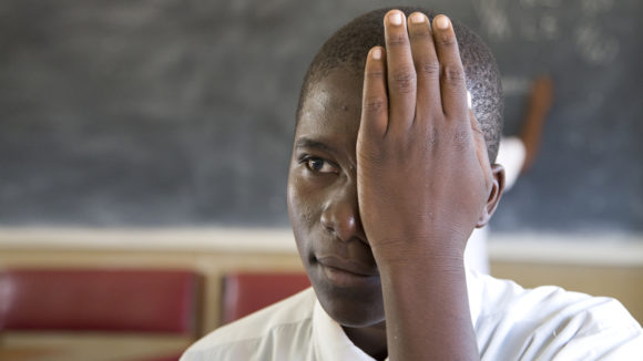 A boy covers one eye with his hand during an eye test.