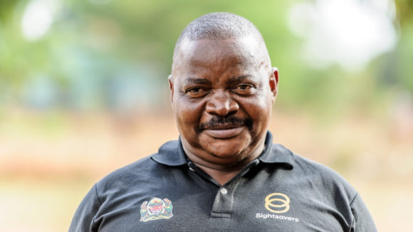 Dr Lukanga wears a Sightsavers-branded top and smiles at the camera.