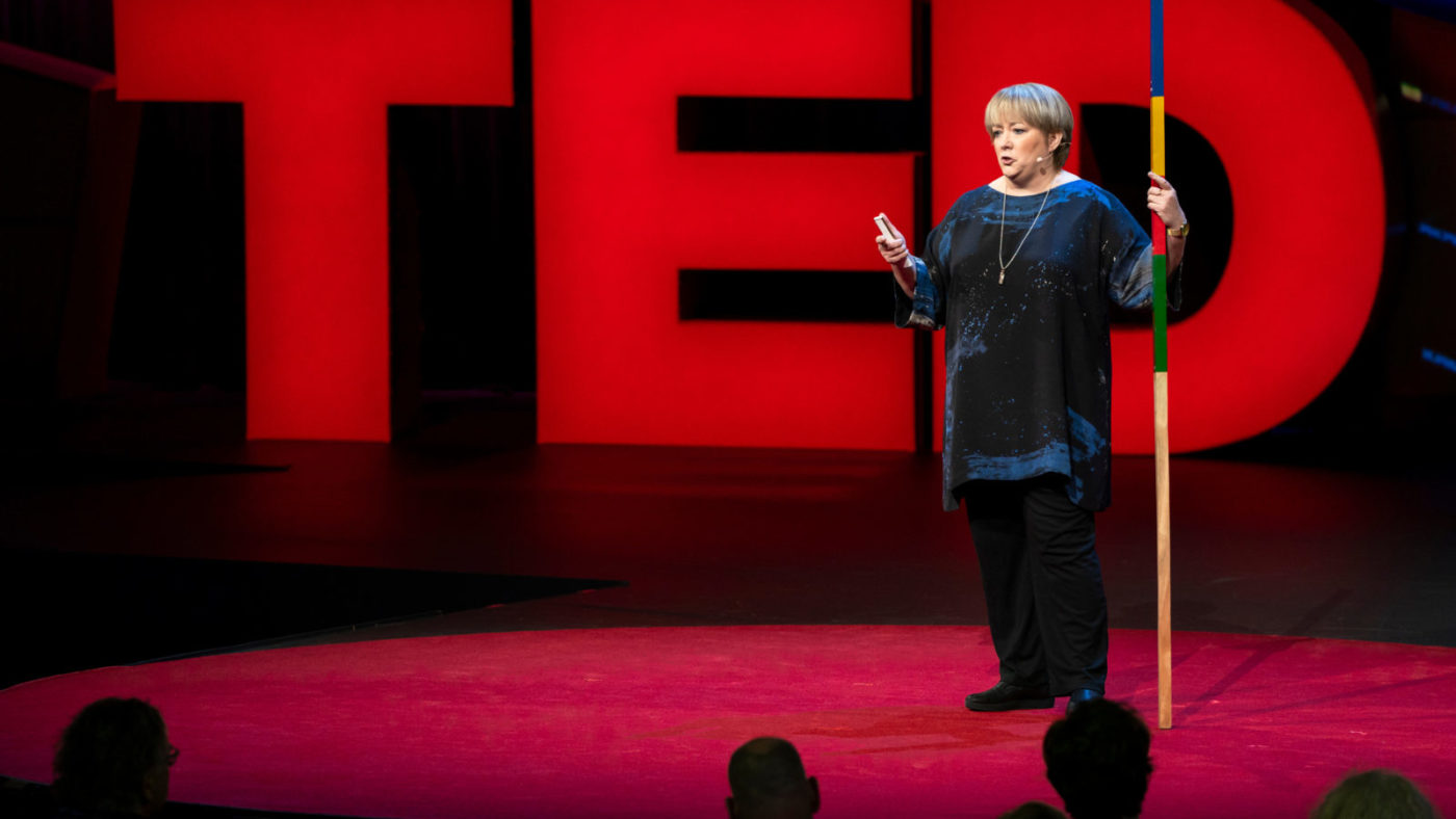 Sightsavers CEO CAroline Harper during her TED Talk, standing in front of large red letters spelling TED.