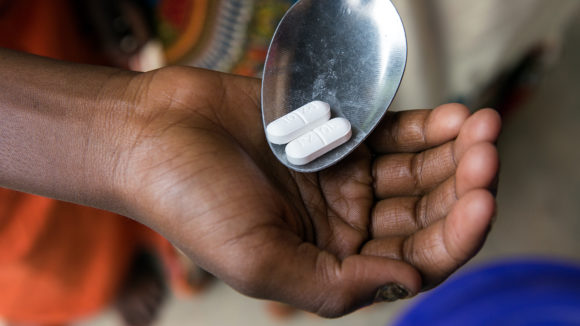 A spoon is used to place two tablets into a child's hand.