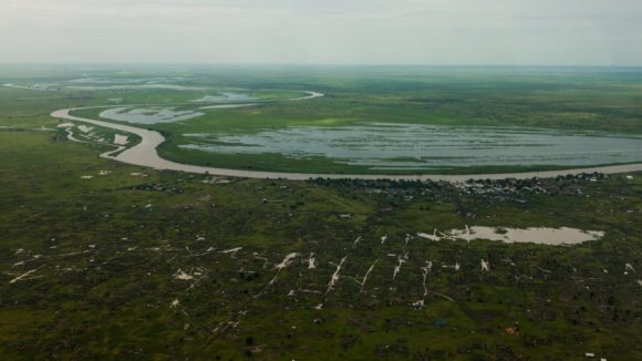 A wide shot of the rural landscape in Nasir, South Sudan. The fields are very wet and the grass is a lush green.
