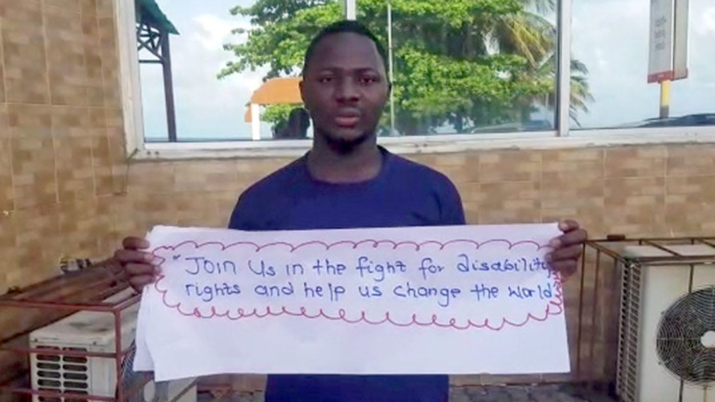 A man holding a sign that reads: Join us in the fight for disability rights and help us change the world.