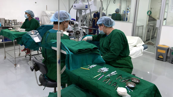 Two surgeons at work in the operating theatre at Mymensingh hospital. They're wearing green scrubs.