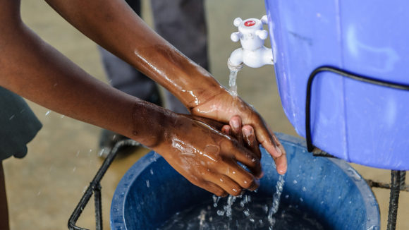 A school student washes her hands using water from a large barrel.