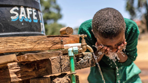 A boy washes his face using water from a tap.