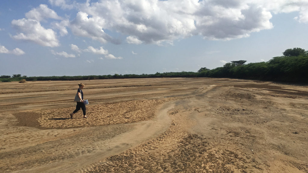 A women walks across a vast dried up river bed.