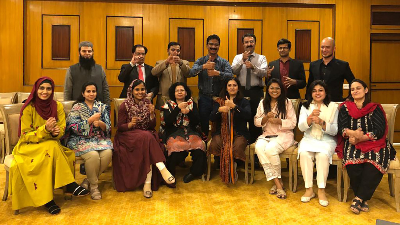 A large group of people pose for a photograph while using sign language.