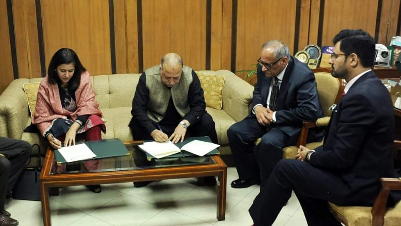 Four people sit in a room. Two of them are signing documents.