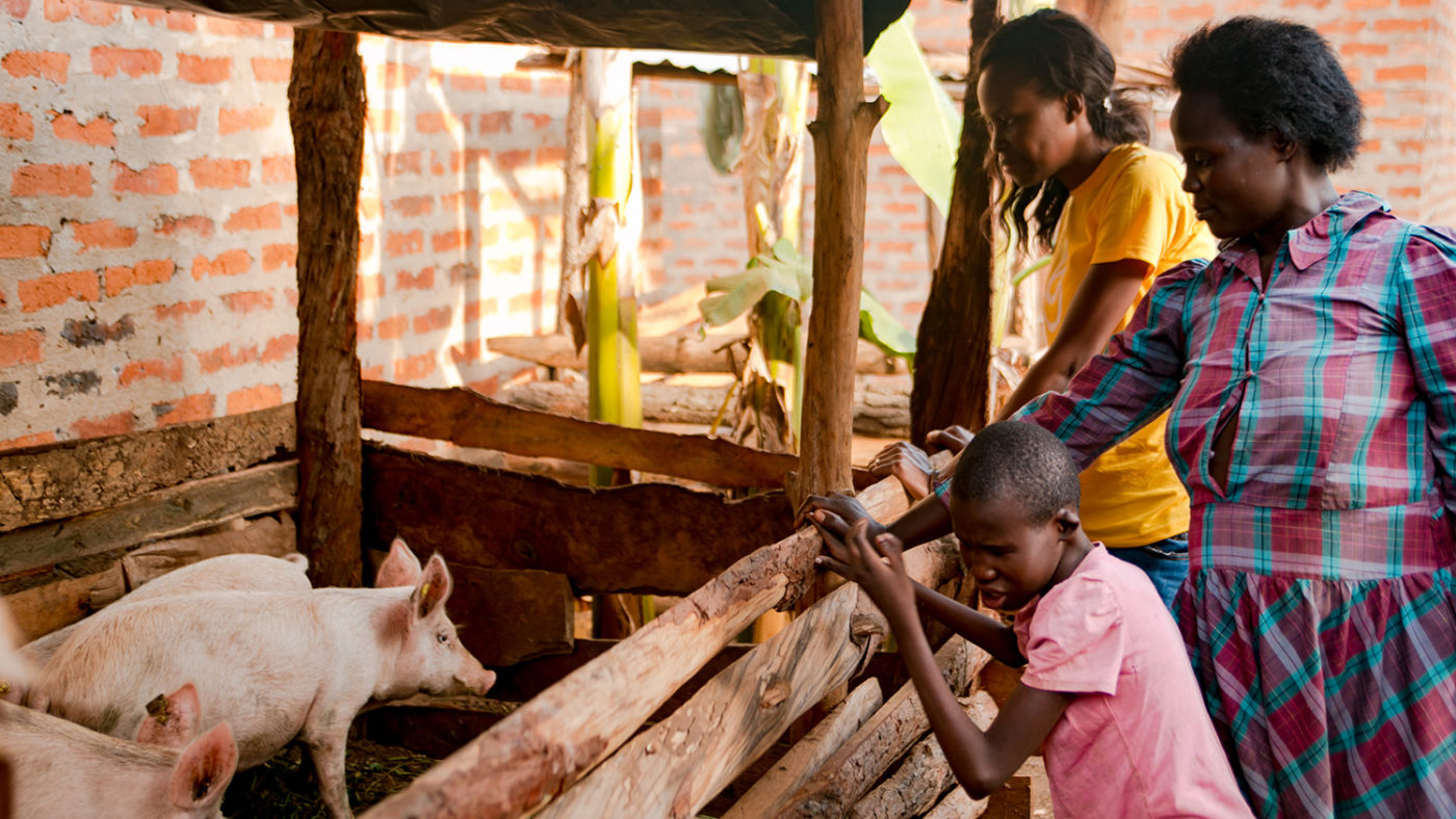 A Sightsavers worker stands with a mother and a child next to a pig pen.