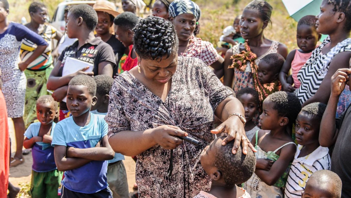 A woman checks a child's eyes for signs of trachoma while a group of children look on.