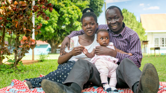 A man and women sit smiling, with their daughter in between them.
