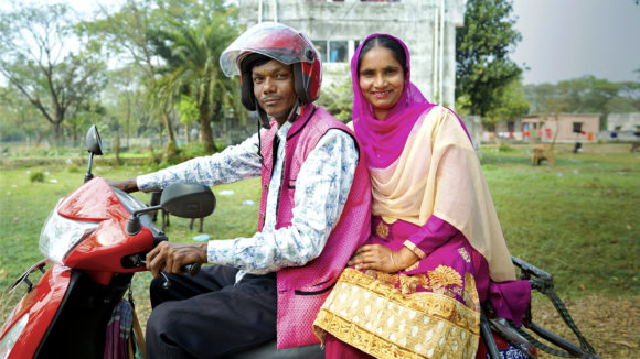 A man and women sat on a motorbike.