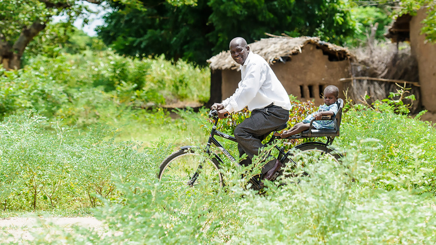 A man riding a bike with a small child behind him in a seat.