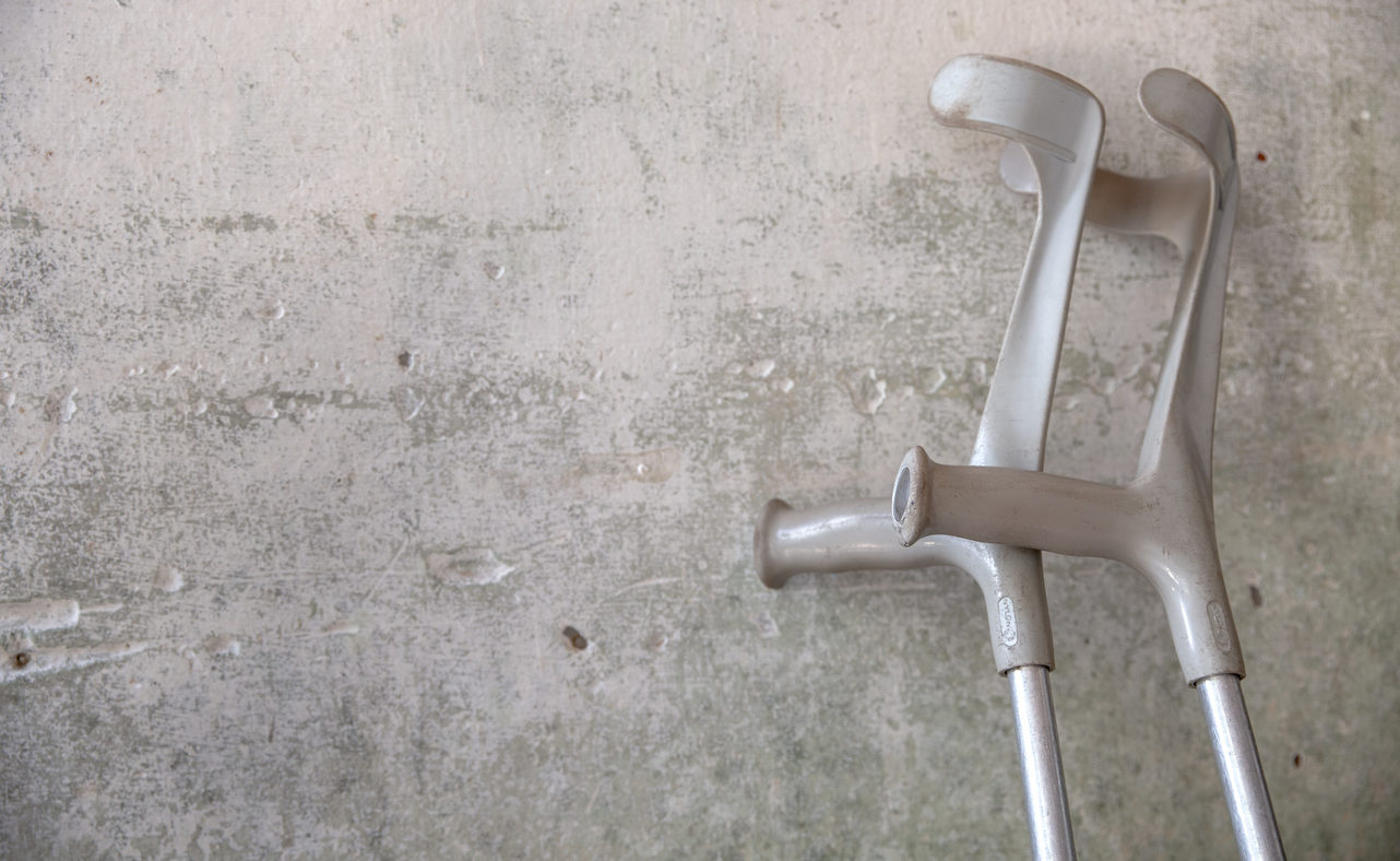 A pair of crutches leaning against a grey wall.