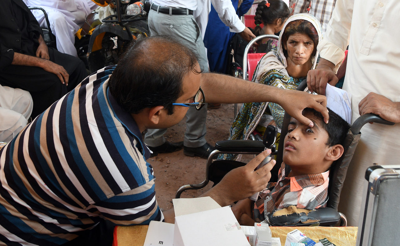 A man examines the eyesight of a young boy who uses a wheelchair.