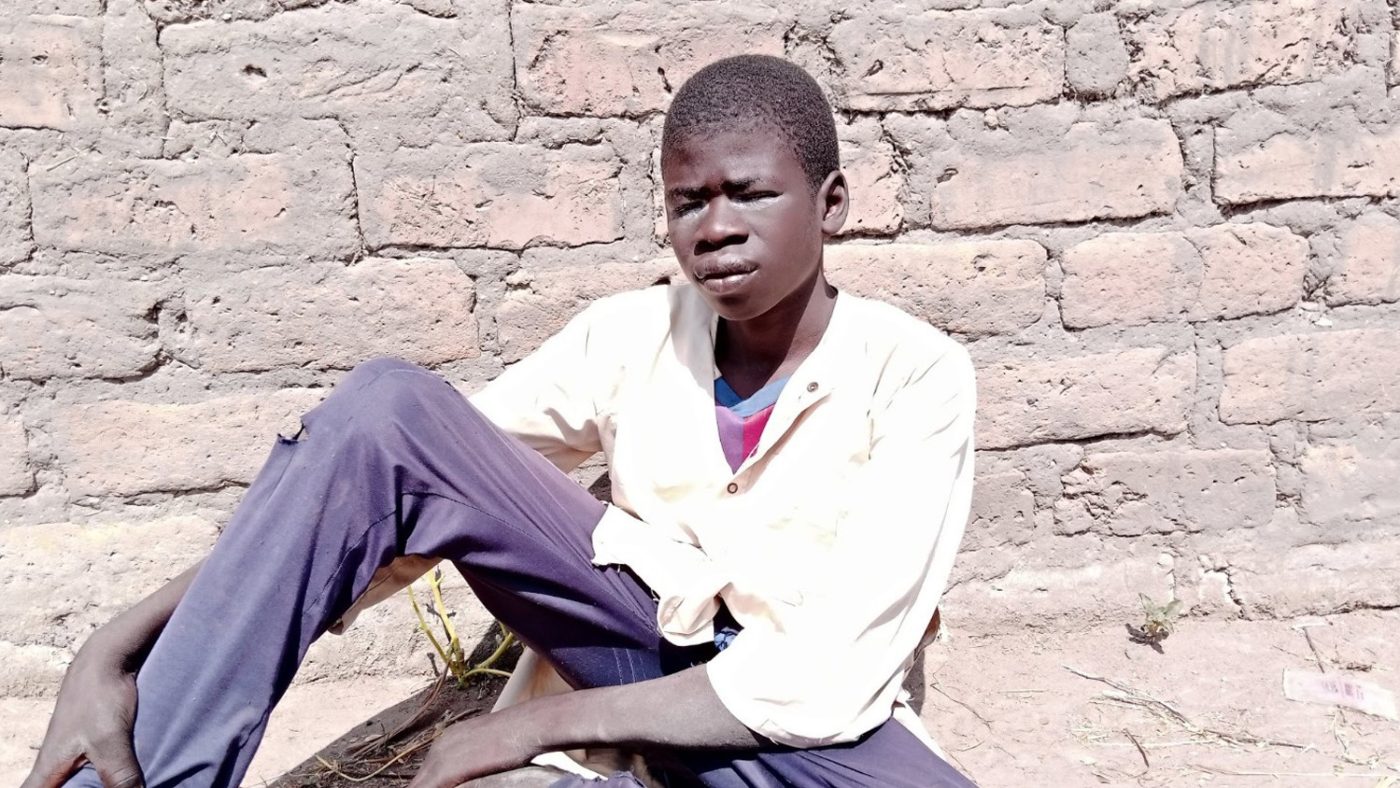 a boy sits next to a wall. his eyes are watery and sore.