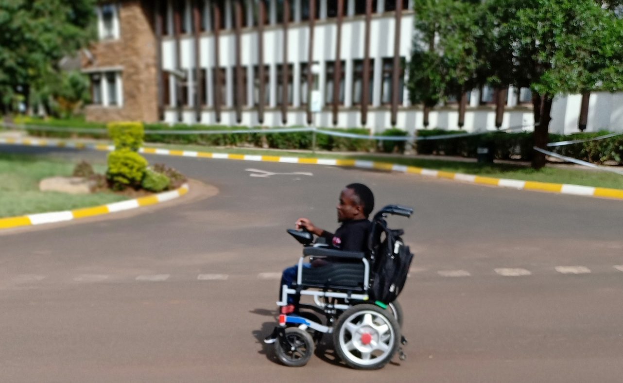 A young man using a wheelchair on a road in Kenya.