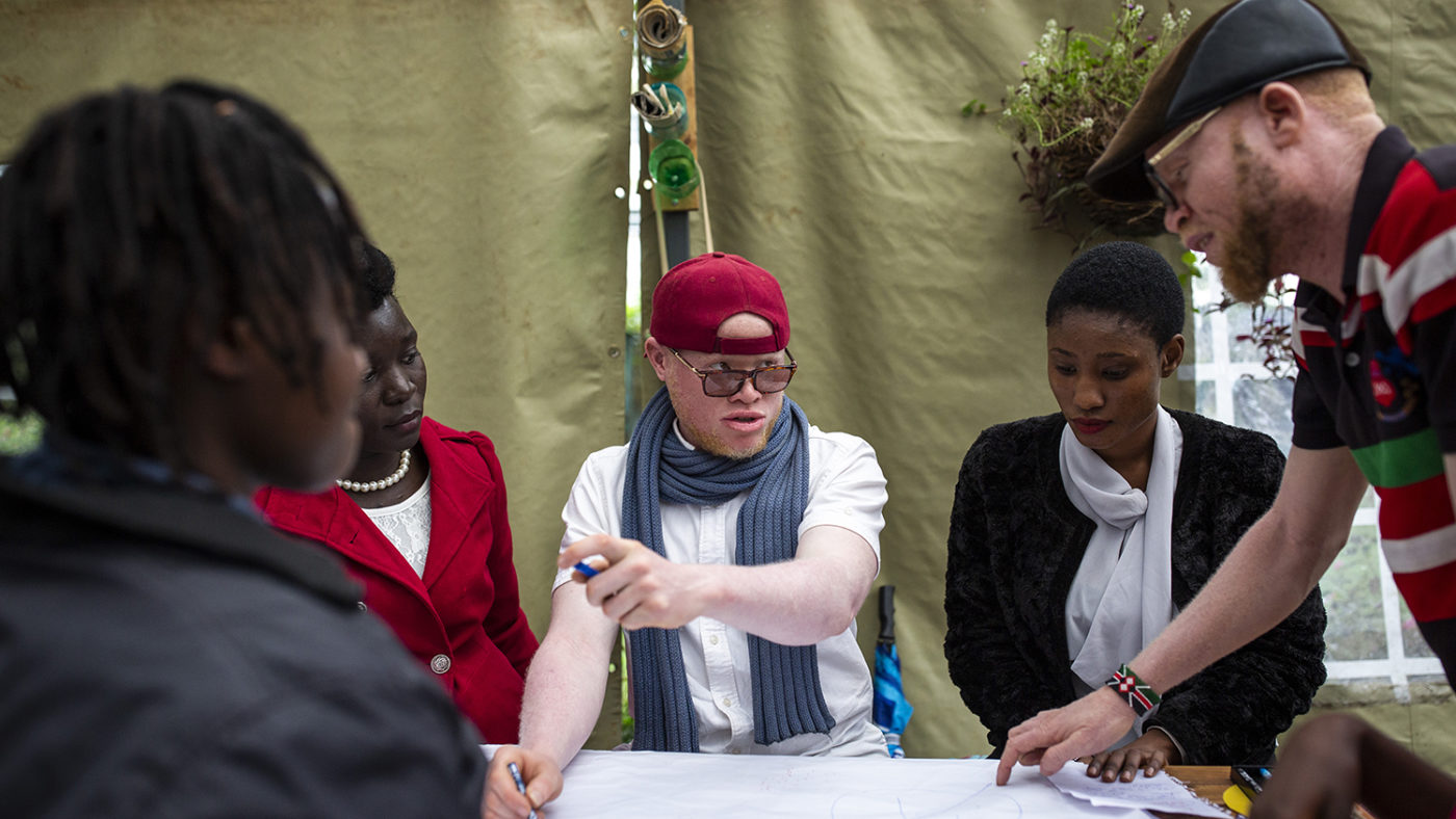 Four people work on a big piece of paper together.