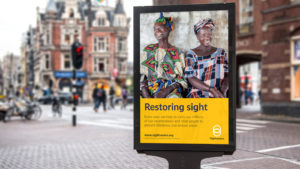 A Sightsavers branded poster displayed on a busy street.