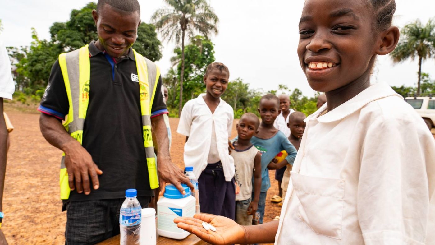 A man distributes treatment to a smiling student.