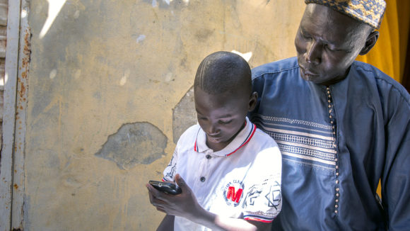 A boy using a phone with his father sitting behind.