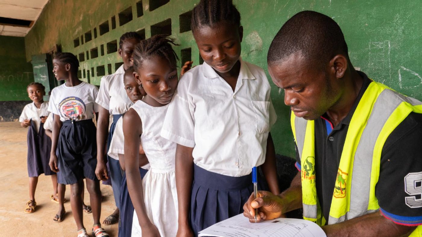 A man writes down the information of students who are waiting to take part in a mass drug administration at school.