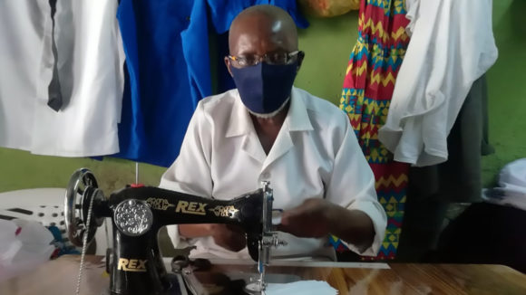 A man working at a sewing machine wearing a face mask.