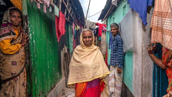 Two Two women and a man stand outside a small home in an informal urban settlement.