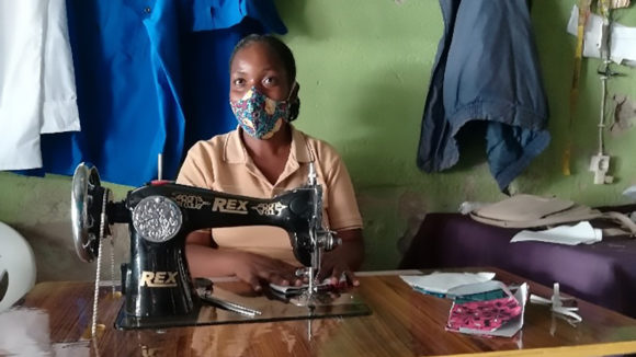 A woman working at a sewing machine wearing a face mask.