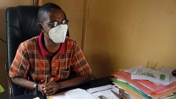 A man sits in an office wearing a face covering