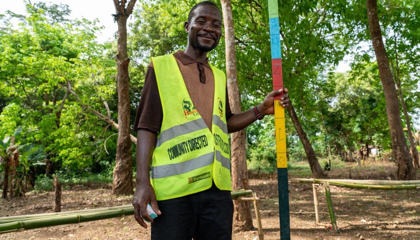 Victor, a community volunteer, stands outside smiling with a dose pole.