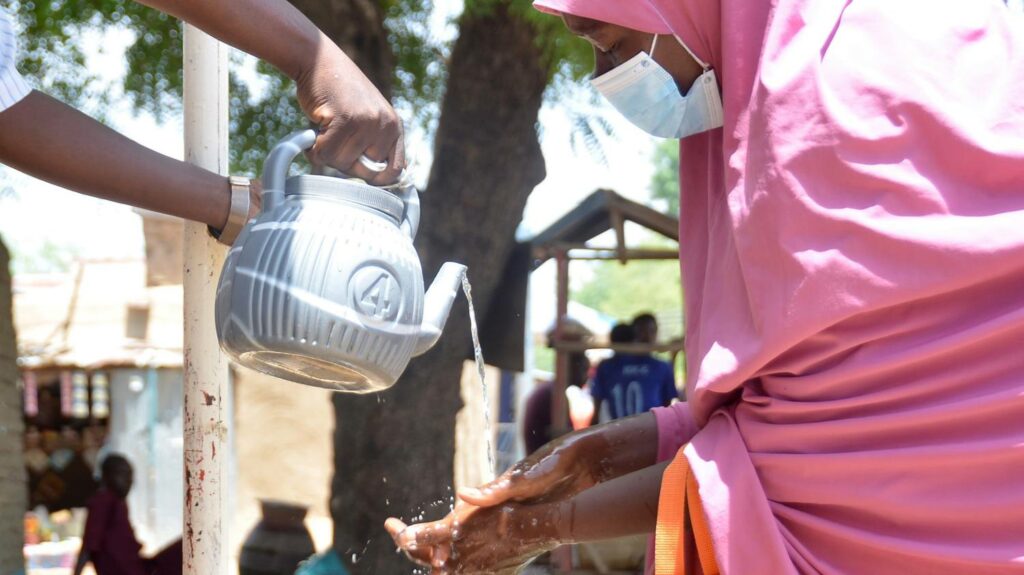 A volunteer drug distributor washing hands washes someone's hands.