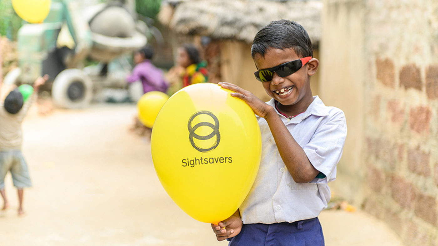 Sanjit holding up a Sightsavers-branded balloon. He is wearing sunglasses.