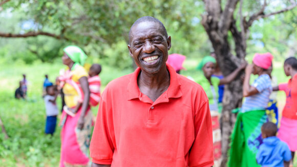 A man smiles while people walk in the background.