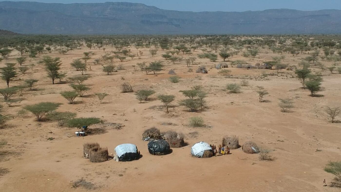 Village with eight structures with backdrop of dry land and mountains.
