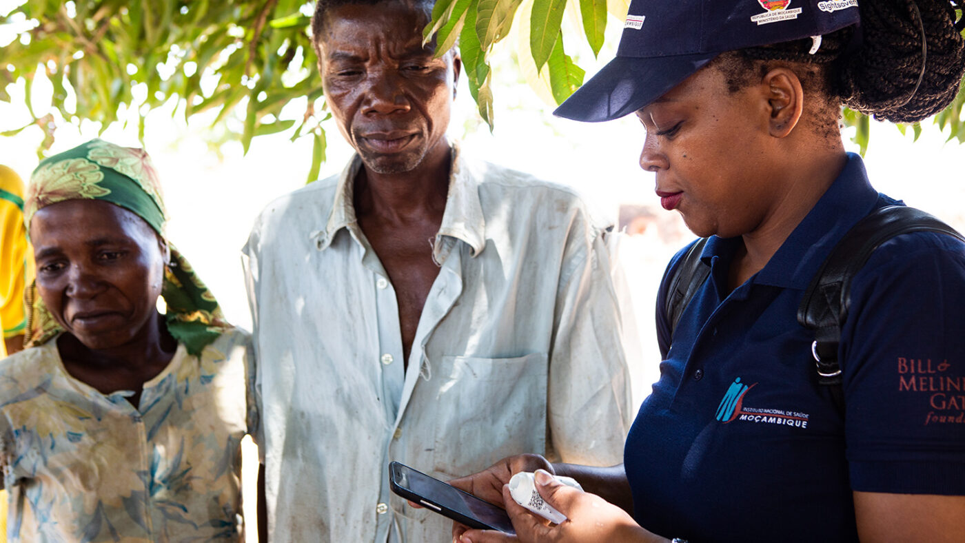 A woman records survey information on a mobile phone app while two survey participant look on.