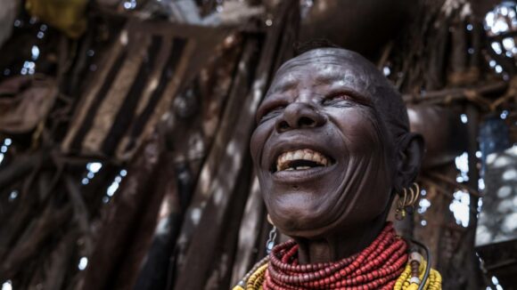 Woman smiles, wearing traditional jewellery, in hut made from branches