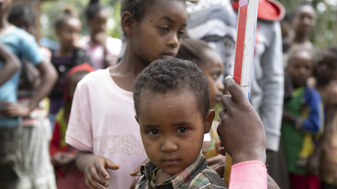 children stand with a dose pole as they are measured for medicine.