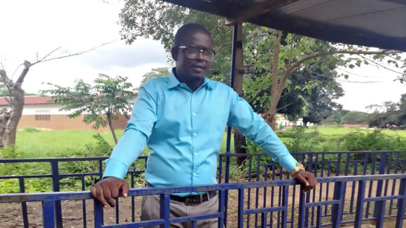 A man wearing a blue shirt stands outside of a school.