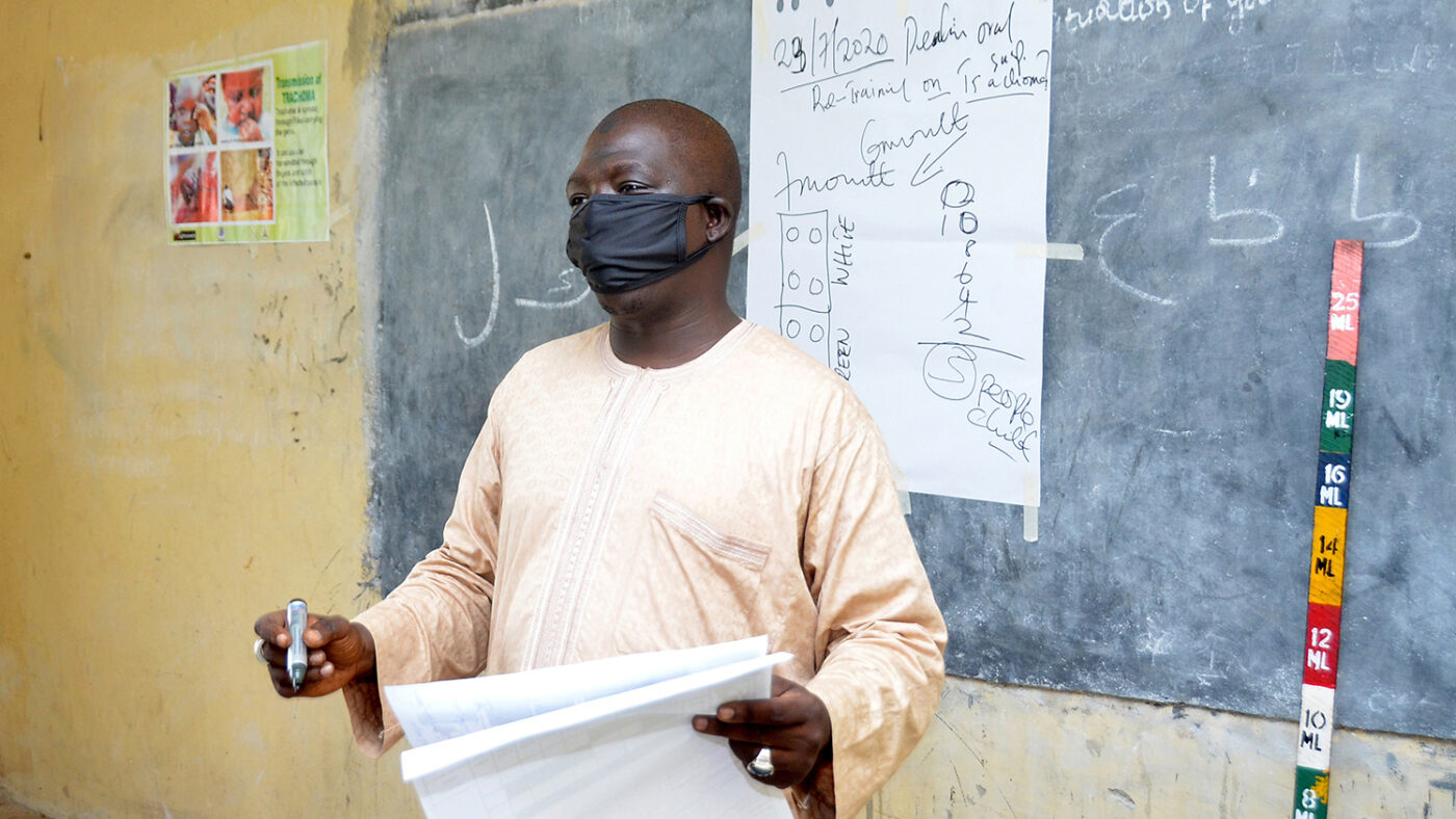 A man, wearing a mask, presents in front of a chalk board during a training.