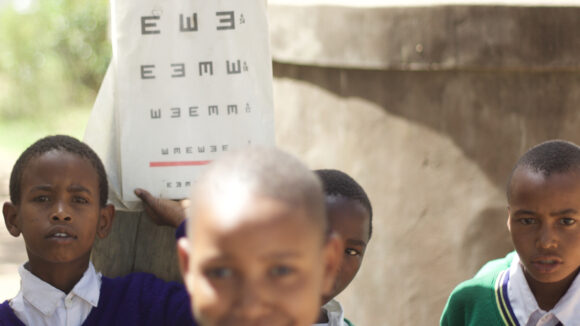 A group of children stand near an eye chart,.