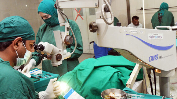 Surgeons in green scrubs lean over a patient during an eye operation.